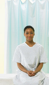 Photograph of a young woman in a hospital gown waiting for a doctor.