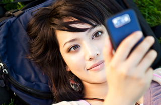 Girl laying on the grass looking up at a cell phone