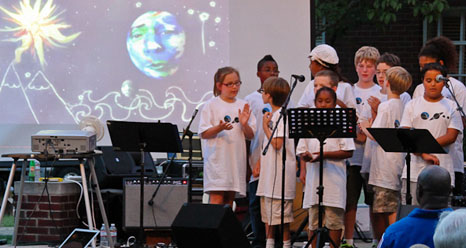 Children in white T-shirts perform for an audience