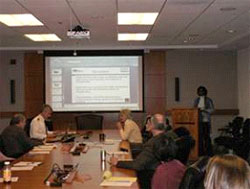 Photograph of attendees gathered around a conference table viewing a presentation.