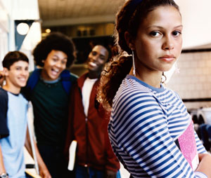 Photograph of a young woman facing the camera while young bullies stand behind her and laugh.