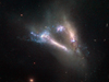 A large, luminous v pointed down to the lower right, shows two edge-on galaxies colliding. Flashes of blue like glitter and distant background galaxies can be seen.