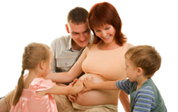 Father, son, and daughter touching the belly of a pregnant mother