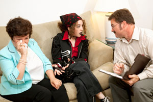 Photograph of a young woman and her mother talking to a therapist.