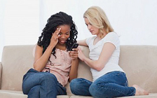 Two women sitting on a couch.  Upset woman is being comforted by the other woman.