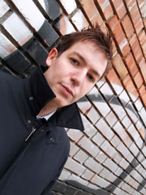 Young man with windblown hair stands in an alley.