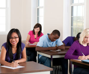 Photograph of teens sitting at desks writing.