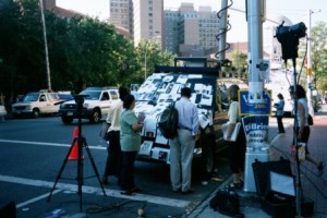 People on street looking at a news van with memorials to victims of 9/11 taped to it.