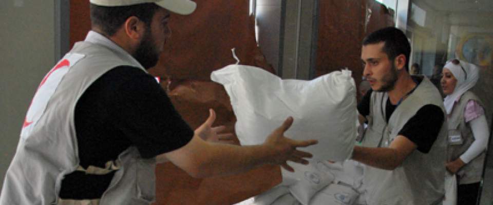 Syrian Red Crescent staff carry sacs of food at a distribution center. AFP Photo/STR 