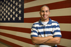 Foto de hombre hispano posando enfrente de una bandera estadounidense