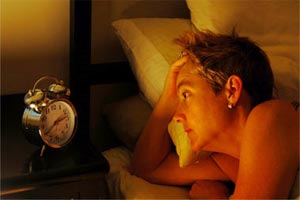 woman in bed staring at an alarm clock
