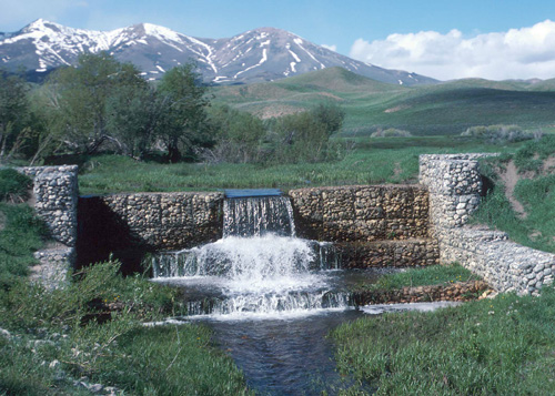 Beautiful image of mountains in the background and stone grade control structure with water flowing