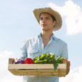 Photograph of a young man wearing a straw hat and carrying a box of produce.