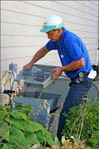Photo of an HVAC professional performing maintenance on an outdoor air conditioning unit. 