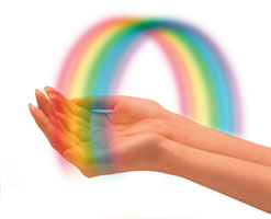 Photograph of two hands with a rainbow arched over them.