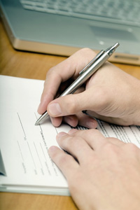 Photograph of a hand using a pencil to fill out a form.