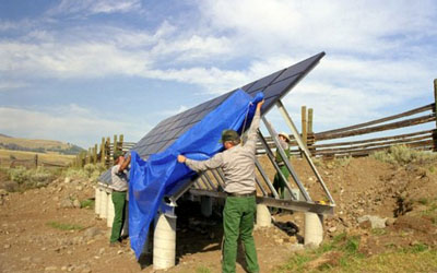 Photo of two men taking a tarp off a new solar panel in the desert.