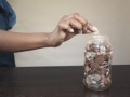 Woman putting coin in savings jar.