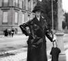 Helen Clay Frick standing, wearing black trench coat, in Belgium.