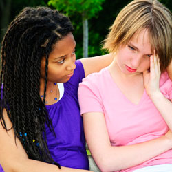 Photograph of a teen girl comforting another, unhappy, teen girl.