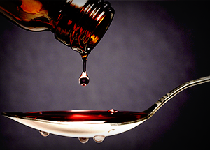  A bottle of cough syrup being poured into a teaspoon.