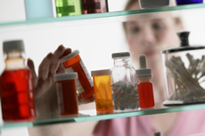 Photo: woman looking into medicine cabinet containing prescription drugs