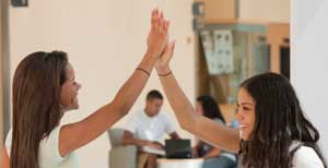 Two young women smile and give each other a high five.