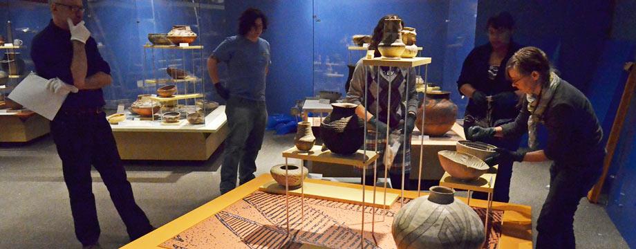 Curators preparing museum gallery with pottery. 