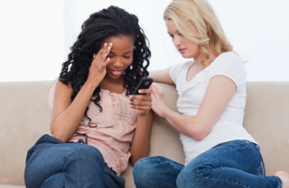 Two women sitting on a couch.  Upset woman is being comforted by the other woman.