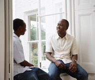 Un padre habla con su hijo adolescente sentados al lado de la ventana.
