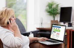 Una mujer sentada con una computadora portátil mirando la página web missingkids.com mientras habla por teléfono.