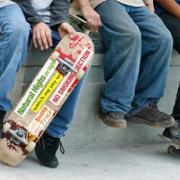 Three teens sitting and one is holding a skateboard