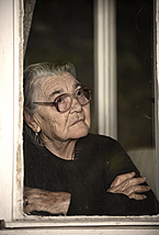 An elderly woman looks out the window