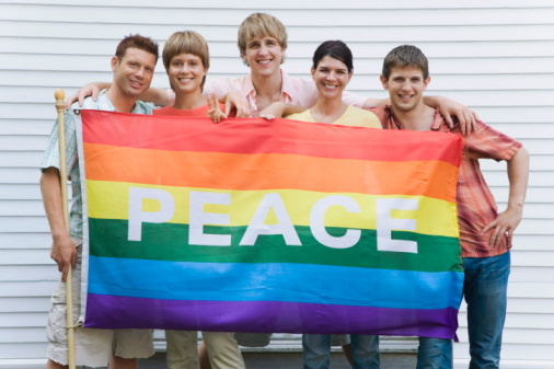 Photograph of young people holding up a rainbow flag with the word Peace on it.