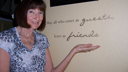 Photo of Anita Bevan next to plaque saying &quot;May all who enter as guests leave as friends.&quot;