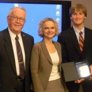 A man and a women presenting an award to a young man.