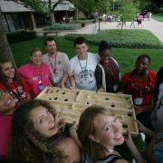 Teens standing in a circle around a board game.