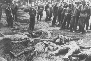 آئن سیٹزکومانڈو (گشتی قاتل اسکواڈ) کے ارکان ایک یہودی نوجوان کو گولی مار کر ہلاک کرنے سے پہلے۔ لڑکے کے مقتول خاندان کی لاشیں اُس کے سامنے پڑی ہیں۔ بائیں طرف لوگ نسلی جرمن ہیں جو اسکواڈ کی مدد کر رہے ہیں۔ سلارو، سوویت یونین، 4 جولائی 1941 ۔