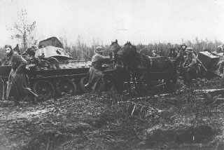 ایک جرمن فوجی دستہ تباہ شدہ سوویت ٹینک کے پاس کیچر میں سے گزرنے کی جدوجہد کر رہا ہے۔