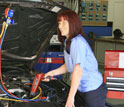 Photo of a smiling young woman working on a car engine.