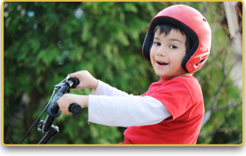 Un niño con casco y camiseta roja anda en bicicleta.