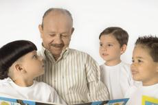 Photograph of a senior man reading a book to three young boys