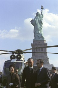 President Lyndon Johnson, Lady Bird Johnson and Bill Moyers behind the Statue of Liberty for the signing of the Immigration Act of 1965. ARC Identifier 2803427