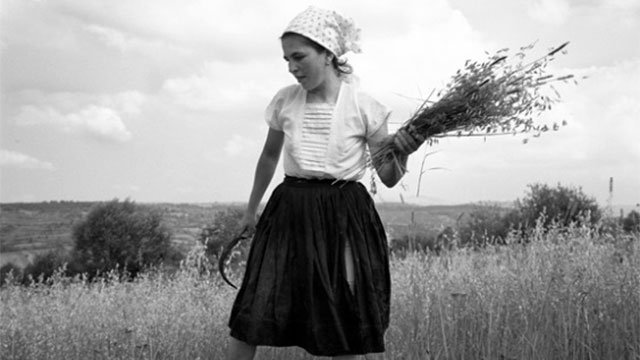 Photo of a woman standing in a field with hay in her hands.