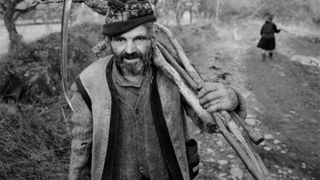 Photo of a man holding sticks and a scythe.