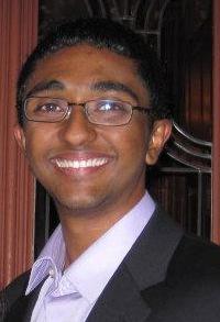 A young man smiling, with glasses.