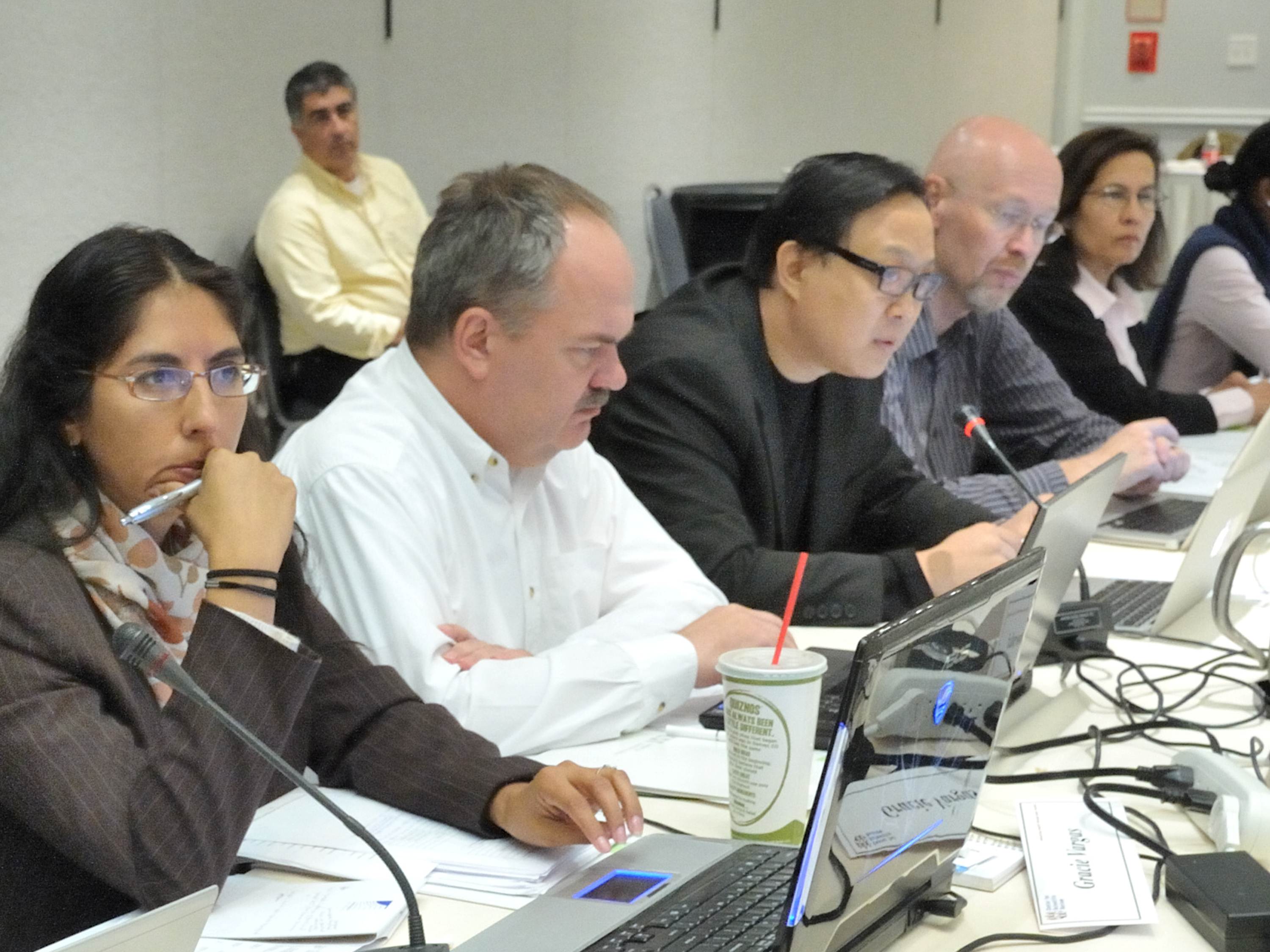 A photo of reviewers at a study section meeting with a NIH program officer sitting in the background