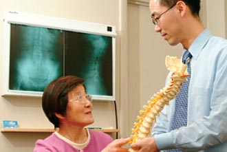 A physician showing a spinal model to an elderly woman