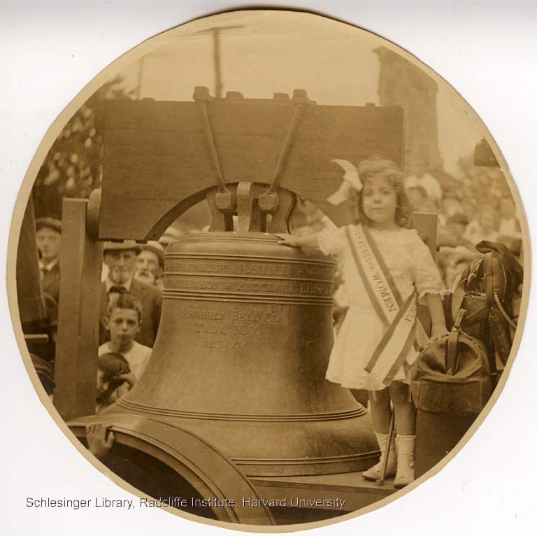 Informal portrait of a young girl standing with the "Justice Bell," a replica of the Liberty Bell, during a suffrage rally in Pennsylvania.