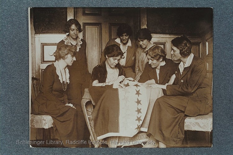 Alice Paul sewing stars on the suffrage flag as others look on, ca.1920.